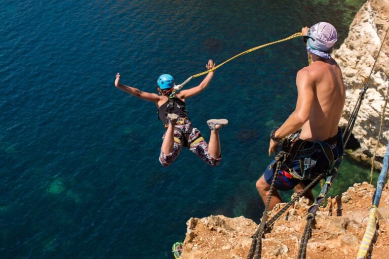 Rope jumping off a cliff with a rope in the water.