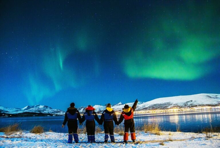 people watching the northern lights close to a lake