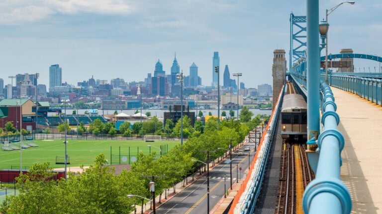 The Philadelphia skyline viewed from across the Delaware River in Camden, New Jersey, with the Benjamin Franklin Bridge spanning the water in the foreground.