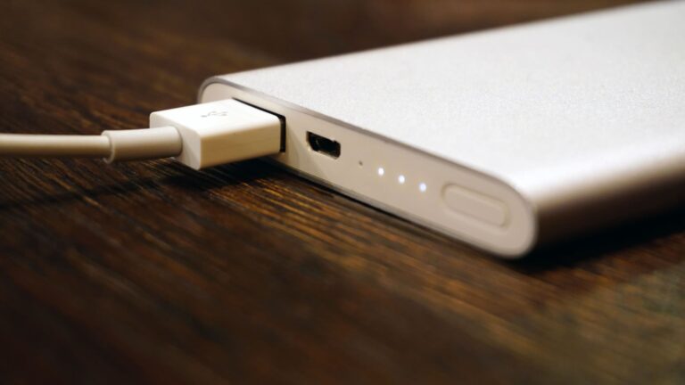 A power bank connected to a smartphone charging on a wooden surface, seen in close-up.
