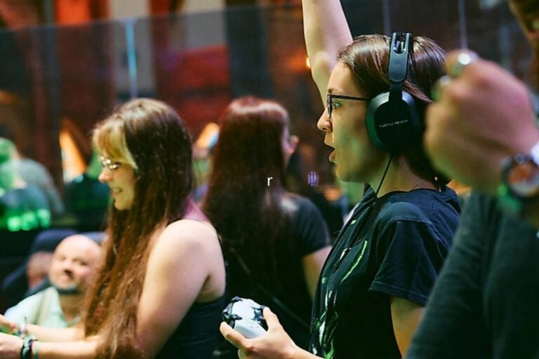 A gamer wearing headphones and glasses holds a controller while playing at Gamescom.