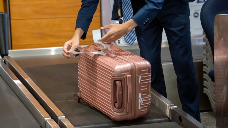 Male airline check-in agent attaching a baggage tag to a passenger's suitcase at Taoyuan Airport
