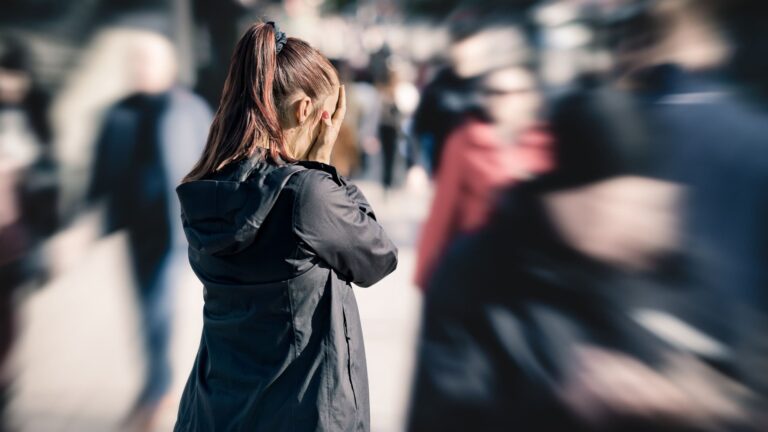 A woman holding her head and looking distressed while standing among a crowd of people.