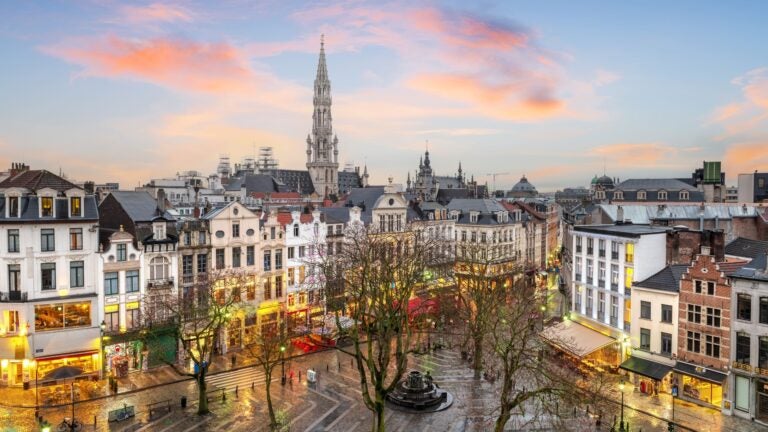 Brussels city square and skyline at dusk, with the illuminated Gothic tower of the Town Hall rising above surrounding rooftops.