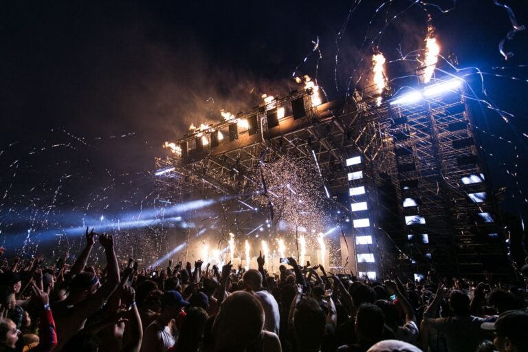 Concert crowd with raised hands watching a stage with flame effects.