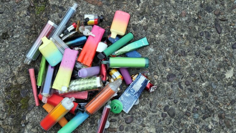 Assortment of used disposable vapes and e-cigarettes grouped together on a worn concrete surface