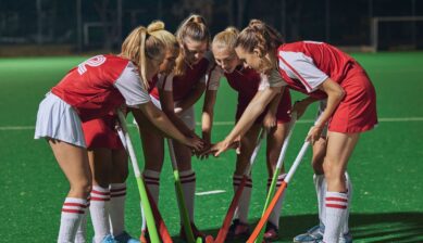 A group of field hockey players stacking their hands together in a circle during a team huddle.