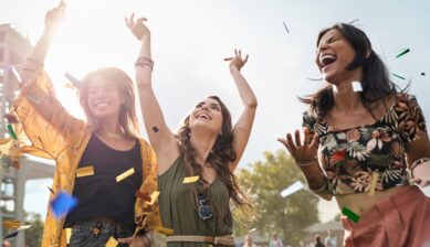 Three friends dancing together at an outdoor music festival on a sunny day