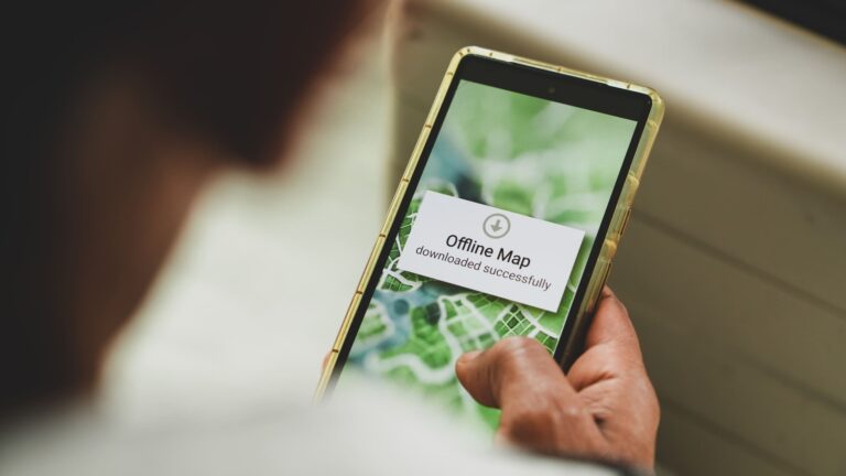 Man holding a smartphone in one hand, downloading an offline map ahead of a trip abroad, with the screen in sharp focus.