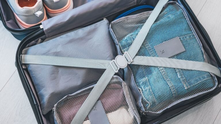 Open suitcase on a pale floor holding neatly arranged packing cubes alongside a pair of shoes