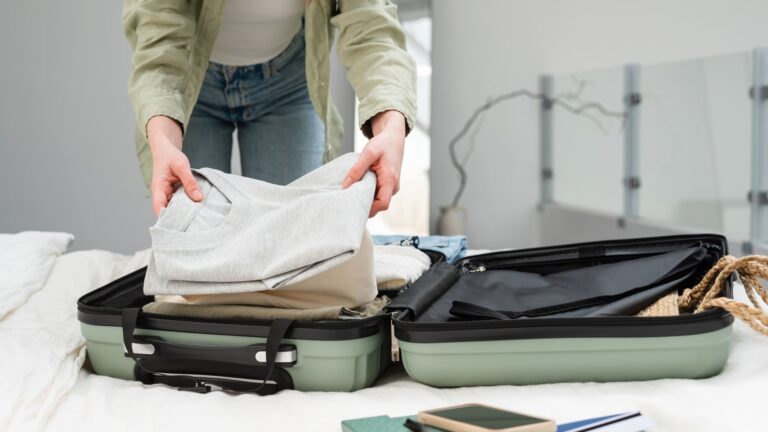 A woman folding clothes into an open suitcase while packing for a trip abroad.