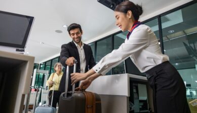 Businessman handing a large suitcase to airline ground crew for weighing at the check-in desk