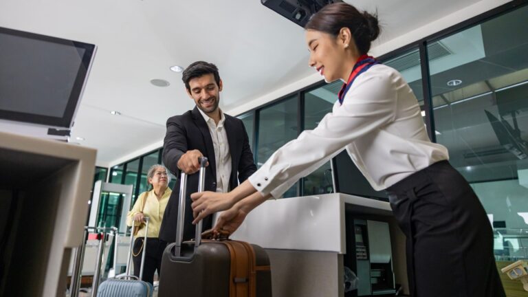 Businessman handing a large suitcase to airline ground crew for weighing at the check-in desk