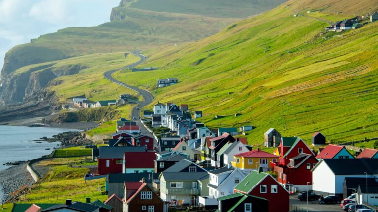 The small village of Sumba on the Faroe Islands, with scattered houses set against steep green hillsides and the surrounding sea