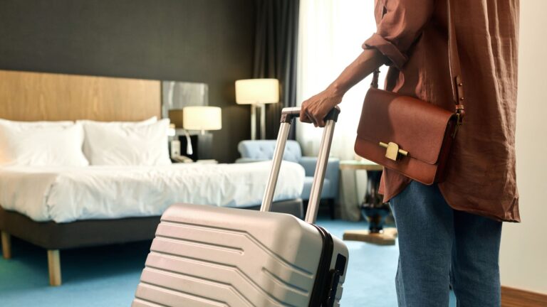 Rear view of a woman wheeling a suitcase as she walks into a hotel room.