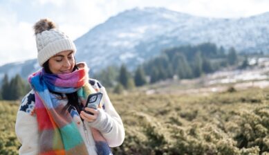 Woman in winter clothing checking her mobile phone on a snow-covered mountainside.