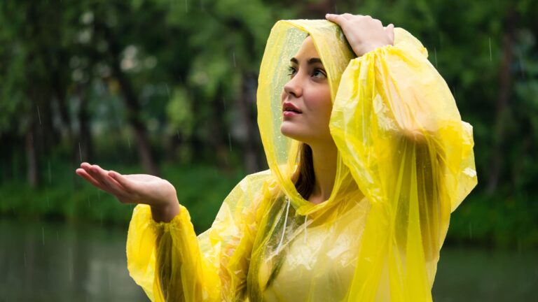 Smiling young woman in a bright yellow raincoat standing out in the rain