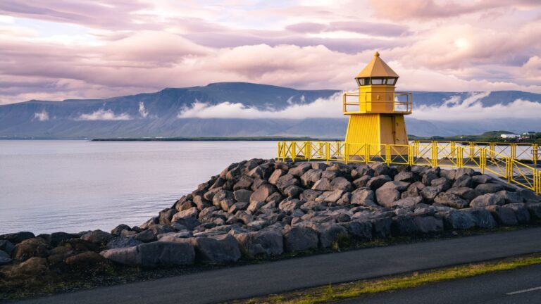 A bright yellow lighthouse standing on the waterfront in Reykjavík, silhouetted against a soft dusk sky