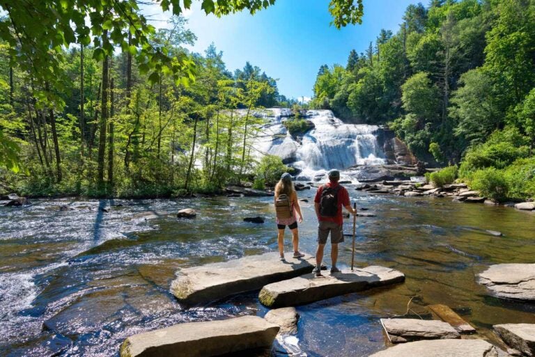 Two hikers standing by a forest waterfall near Asheville, North Carolina.