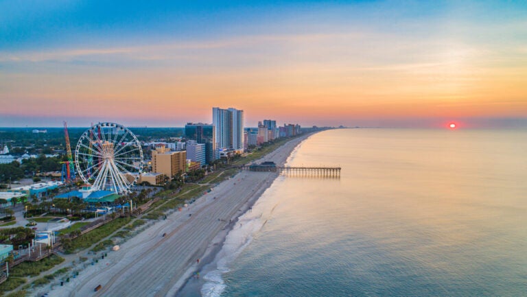 Aerial view of Myrtle Beach, South Carolina, with the coastline, pier, and Ferris wheel at sunset.