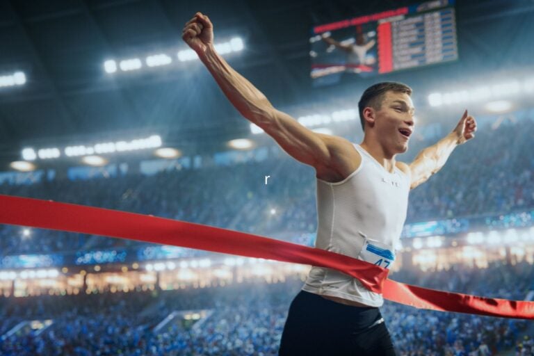 Male runner celebrates as he crosses the finish line in a packed stadium.