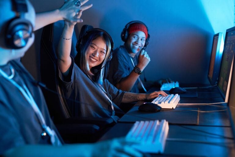 Esports players wearing headsets celebrate together at gaming computers.