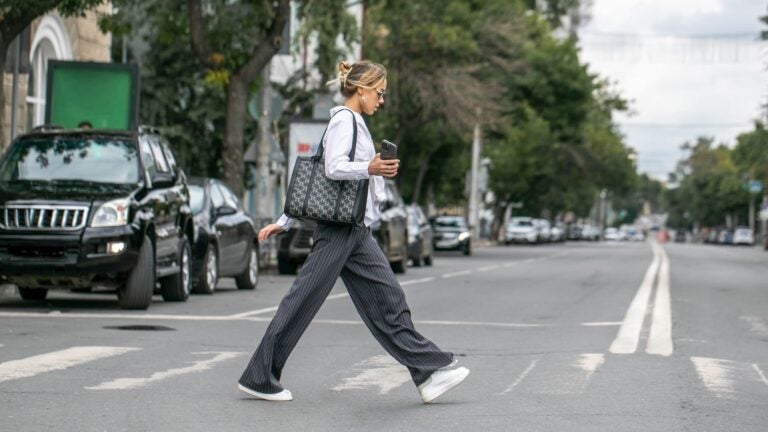A young woman in business attire walking across a city street away from a marked pedestrian crossing.