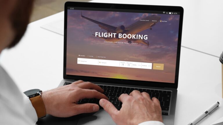 Close-up of a man booking a flight on a laptop at a white desk