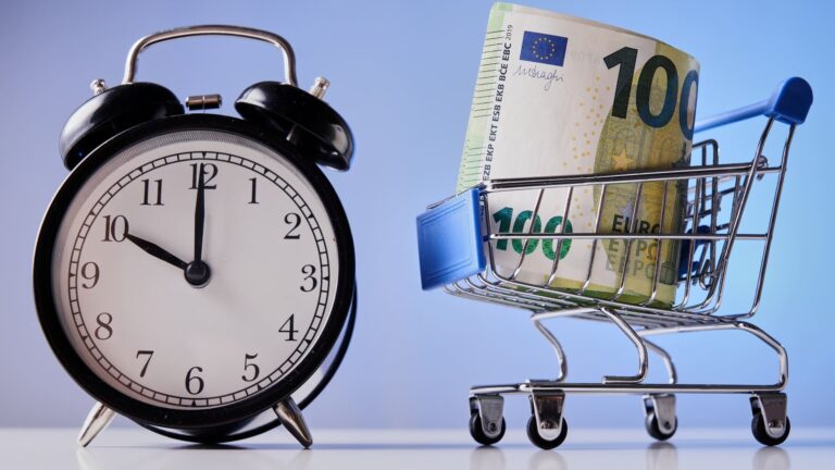 A shopping cart holding a 100 euro note next to a clock set to ten o'clock.