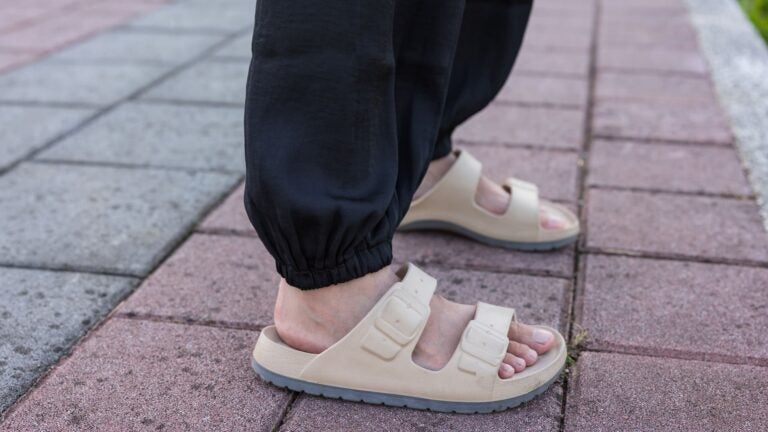 Close-up of a traveler's feet in beige open sandals walking along a paved outdoor path