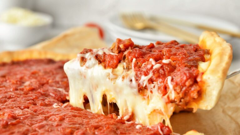 A close-up slice of Chicago deep dish pizza showing a thick buttery crust, a layer of cheese, and chunky tomato sauce on top.