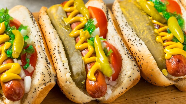 A Chicago-style hot dog on a poppy seed bun loaded with yellow mustard, green relish, chopped onions, tomato slices, a dill pickle spear, and sport peppers.