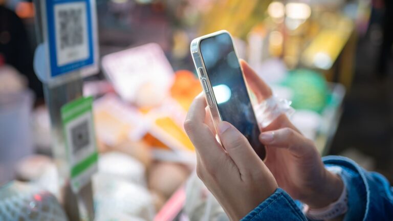 A traveler scans a QR code with a smartphone to pay at a crowded nighttime street food market in China.