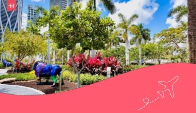 Sunny urban park in Miami with palm trees, colorful animal sculptures, landscaped gardens, and high-rise buildings in the background.