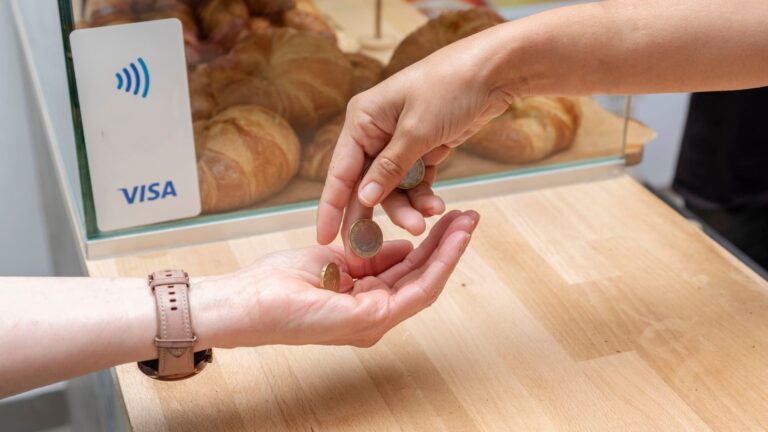 Coins being passed from one person's open palm into another's hands during a cash transaction.