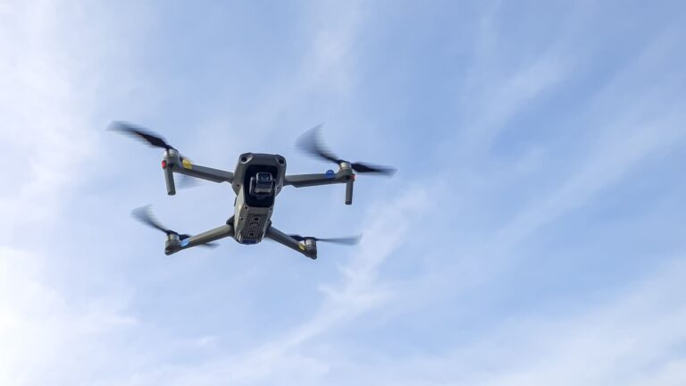 A white quadcopter drone hovering against a clear blue sky