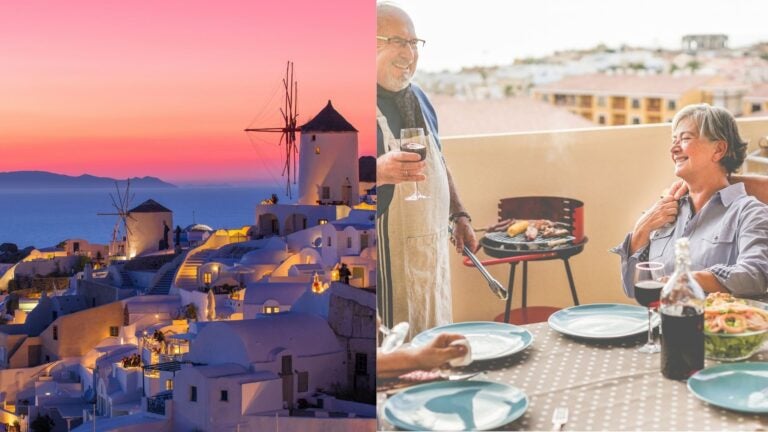 Greek windmills at sunset beside an older couple enjoying a meal on a terrace.