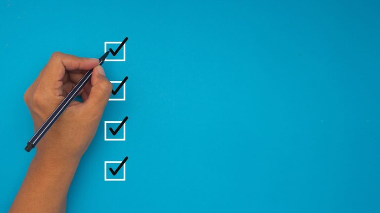 A hand holding a pen marking check marks inside boxes on a blue checklist.
