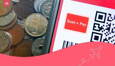 A smartphone displaying a QR code payment screen next to a pile of Japanese yen coins