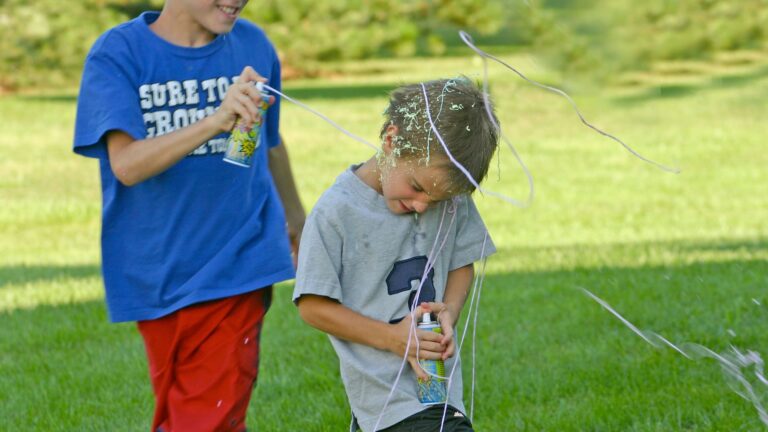 Two boys spraying colorful cans of string at each other while playing outdoors.