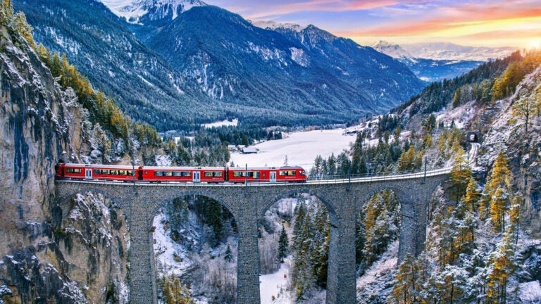A train crossing the curved Landwasser Viaduct through snowy alpine terrain near Filisur, Switzerland