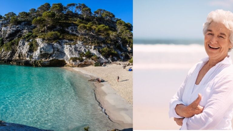Retired woman beside a secluded Menorca cove with turquoise water and pine-covered cliffs.
