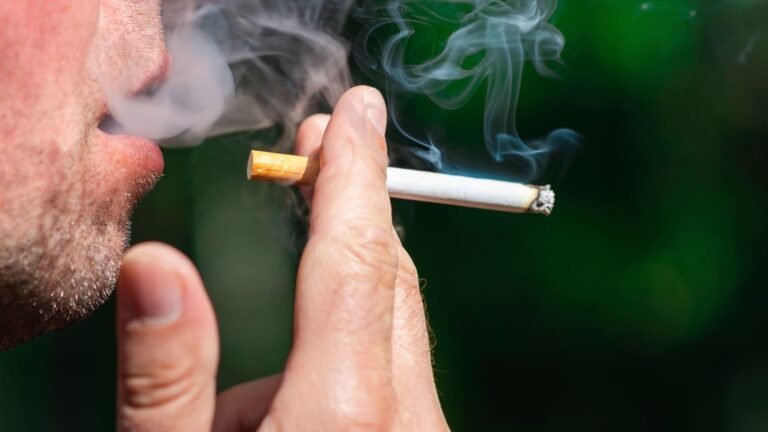 Close-up of a man smoking a cigarette outdoors against a blurred green background
