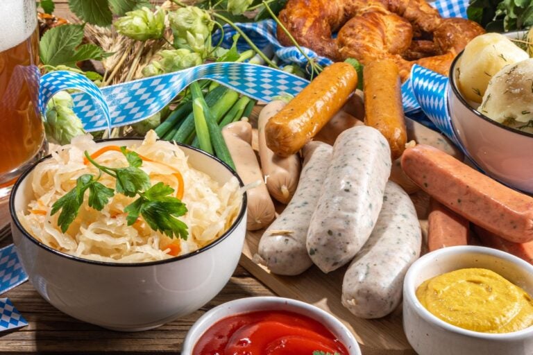 Traditional Oktoberfest festival food, bavarian sausages, pretzels, potato, sauerkraut, beer mug on wooden background