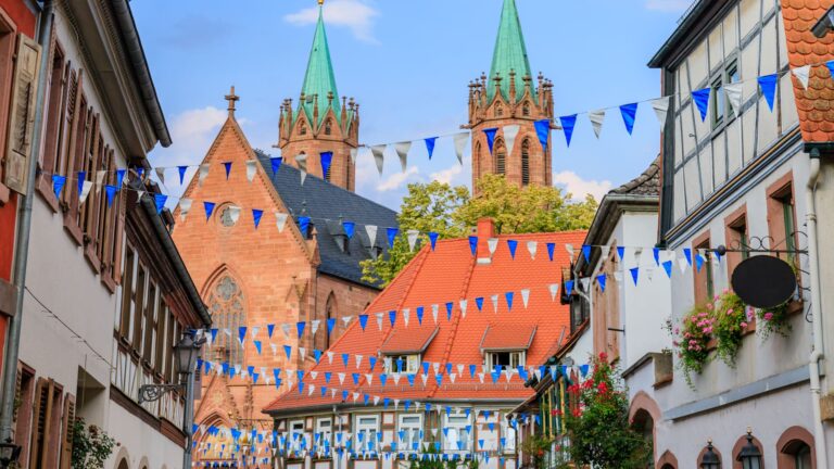 A street in an old German town lined with traditional timber-framed houses and strung with festive Oktoberfest garlands.