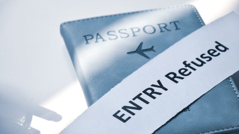A passport beneath a torn scrap of paper stamped "Entry refused," illustrating a traveler being denied entry at a border.