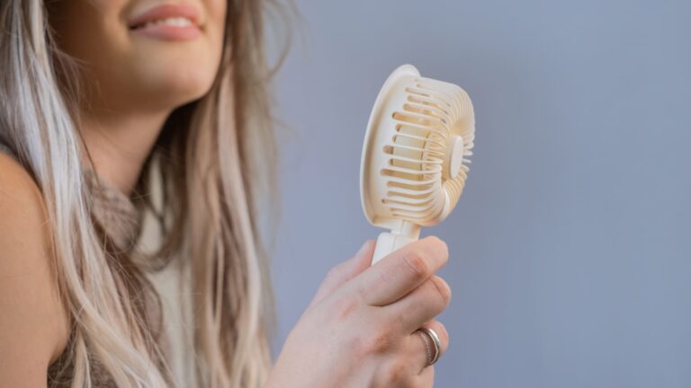 Young woman holding a small handheld electric fan up to her face outdoors on a sunny day