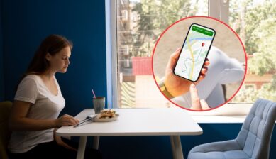 A woman eats a sandwich alone at a table by a window, with an inset circle showing a hand holding a phone that displays a map navigation app.