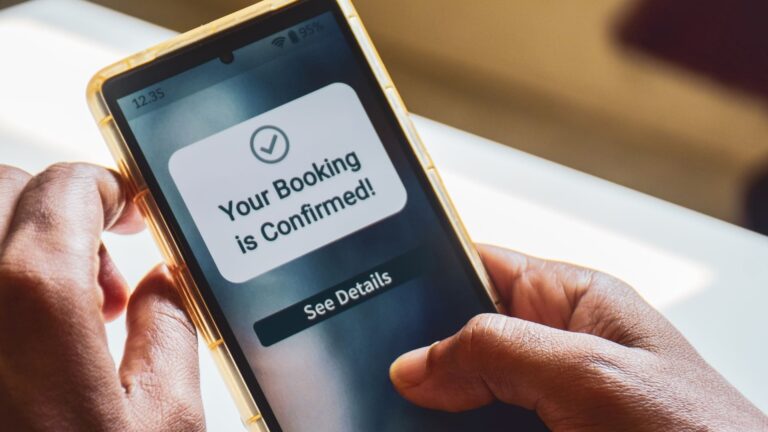 Man holding a smartphone showing a "Your booking is confirmed" travel notification