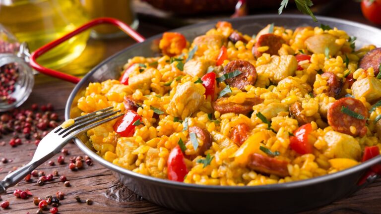 Traditional Valencian paella with chicken served in a pan on a rustic wooden surface, viewed from above